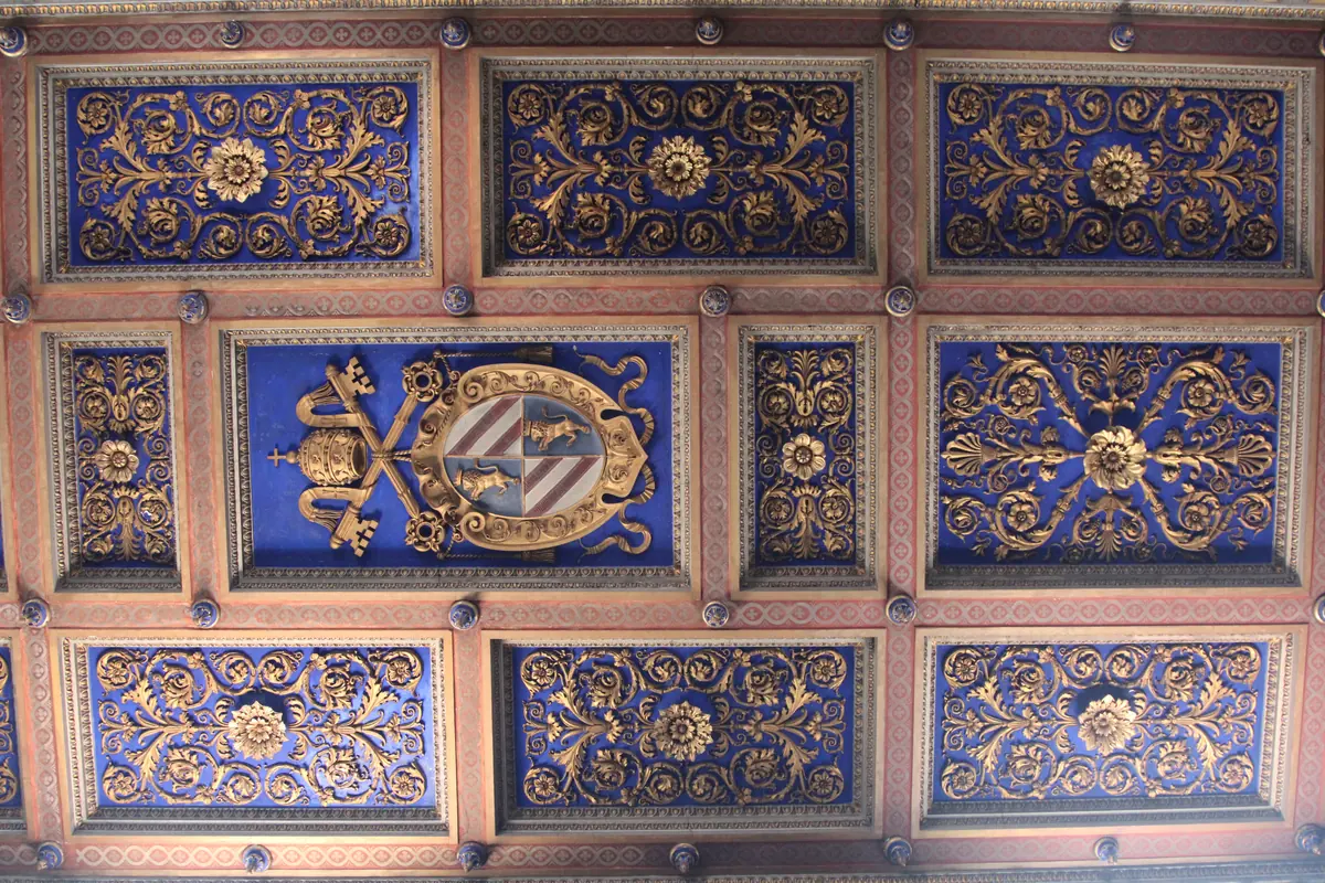 The coffered ceiling of San Nicola in Carcere: blue panels with gilded foliage and a central coat of arms with papal keys
