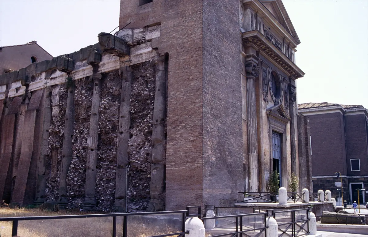 Ancient temple columns built into the brick side wall of San Nicola in Carcere, with the church façade and bell tower at the right
